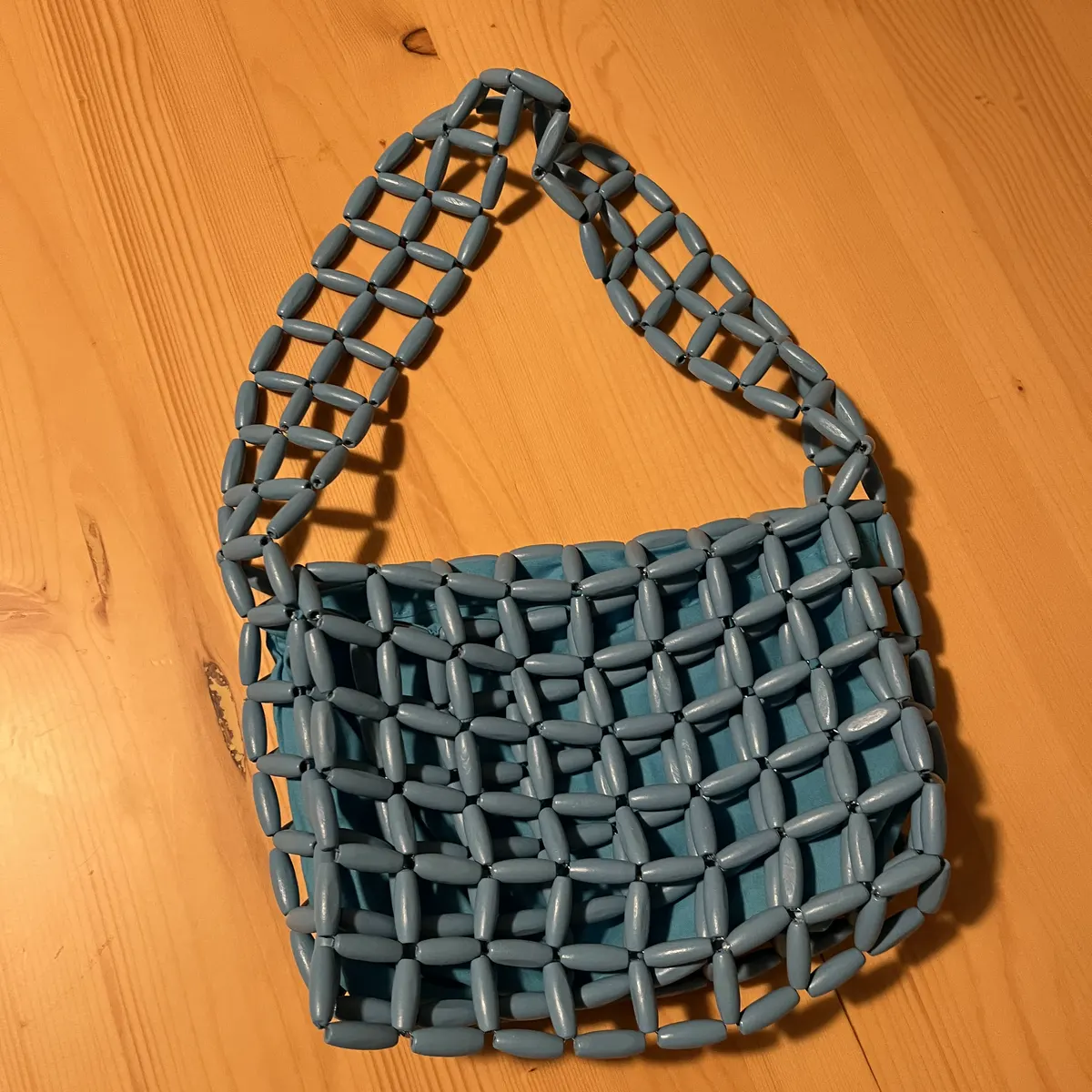 Phone photo of a handmade blue woven bag on a wooden table, before editing
