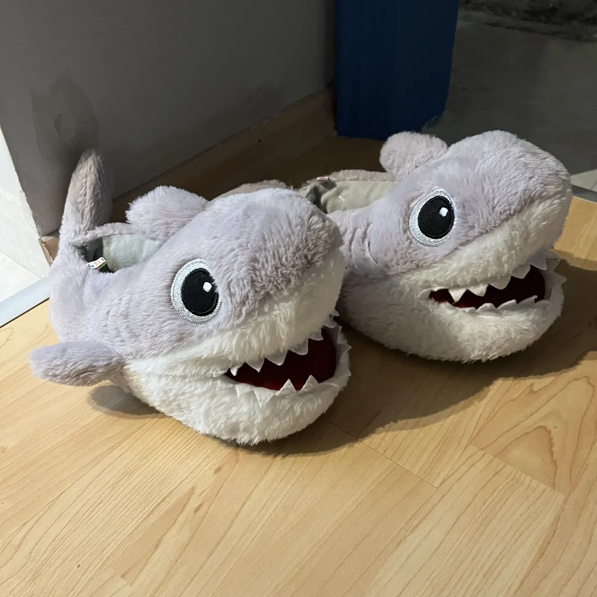 Phone photo of plush shark slippers on a wooden floor, before editing